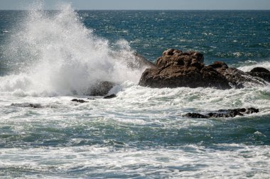 Güçlü dalgalar kıyı şeridi boyunca kayalara çarparak sisli bir sprey oluşturur..