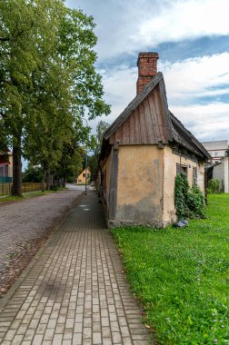 An old house with a slanted roof sits alongside a paved walkway in a peaceful village. clipart