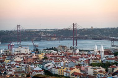 Lizbon, Portekiz - 10 Eylül 2024: Uzaktaki köprüleri ve kıyı sularıyla Lizbon şehir manzarası üzerinde gün batımı manzarası