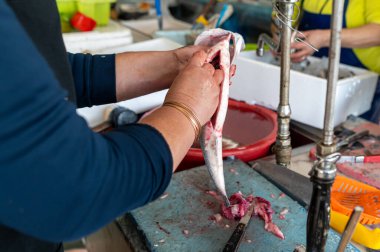 Bir satıcı, yoğun bir pazar ortamında iş yüzeyinde ustalıkla balık temizler..