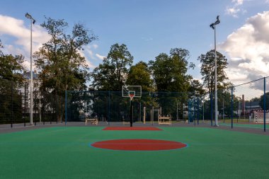 Parktaki geniş bir basketbol sahası, ağaçlarla çevrili, gün batımında sessiz..