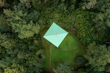 Etrafı sık orman yeşillikleriyle çevrili bir gözlem kulesinin havadan görüntüsü.