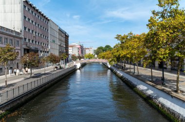 Aveiro, Portekiz - 11 Eylül 2024: Sakin bir kanal, canlı ağaçlar ve şehir binalarıyla çevrili iken mavi gökyüzünü yansıtır.