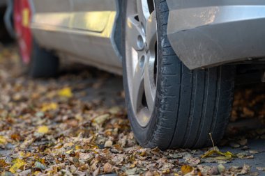 Patlak lastikli gümüş bir araba yere düşen sonbahar yapraklarıyla çevrilidir..