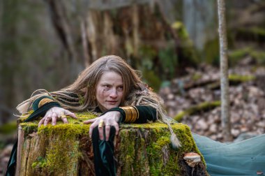 Bir kadın ormandaki yosun kaplı bir ağaç gövdesine yaslanıyor. Suyun sığ derinliği