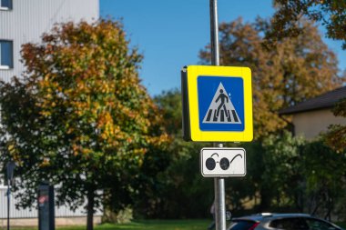 Güneşli bir sonbahar gününde etrafı renkli ağaçlarla çevrili yaya geçidi tabelası.