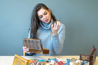 Masada bir sürü mücevherle oturan ince esmer, farklı mücevherler seçiyor ve deniyor.