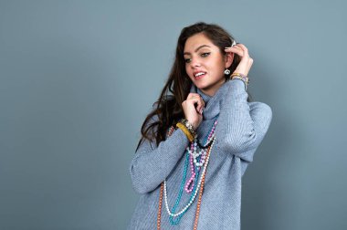 Uzun gri kazaklı sıska kadın, gri renkli kolye ve mücevherlerle eğleniyor.