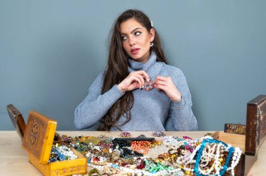 Masada bir sürü mücevherle oturan ince esmer, farklı mücevherler seçiyor ve deniyor.