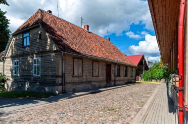Tukums, Letonya - 22 Ağustos 2024 Güneşli bir günde ahşap bir ev kaldırım taşı yolunun yanında duruyor.