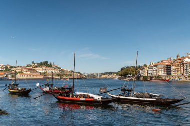 Porto, Portekiz - 12 Eylül 2024: Arka planda Porto 'nun silueti olan geleneksel teknelerin Douro Nehri üzerindeki manzarası