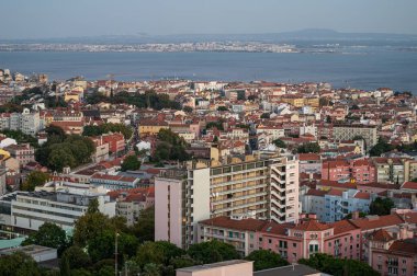 Lizbon, Portekiz - 10 Eylül 2024: Değişik mimari ve sakin suların gün batımında sergilendiği canlı kent manzarası.