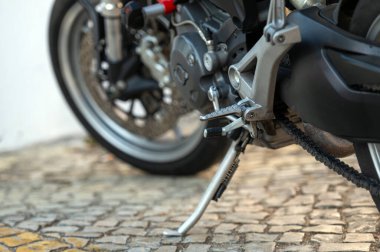 The kickstand of a motorcycle rests firmly on rustic cobblestones under clear skies. clipart