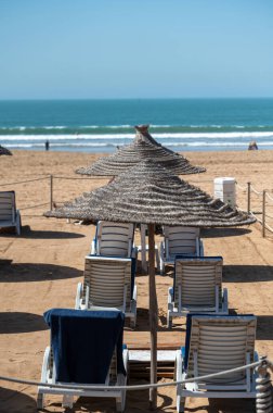 Fas sahilinde, okyanus manzaralı saman şemsiyelerinin altına dizilmiş güneş şezlongları..