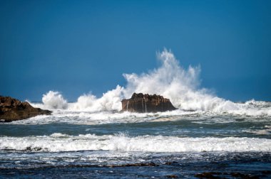 Dalgalar, açık mavi gökyüzünün altında, Essaouira, Fas kıyıları boyunca kayalıklara çarpar.