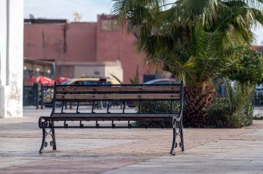 Boş bir bank, öğlen saatlerinde kalabalık Marakeş 'teki yemyeşil bitkiler tarafından çerçevelenir..