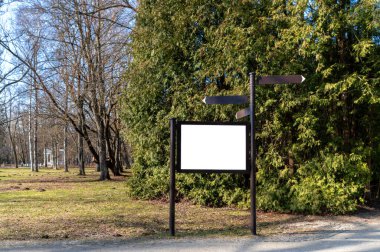 Baharda açık ve güneşli bir günde ağaçlarla çevrili bir parkta yön tabelası duruyor. Model