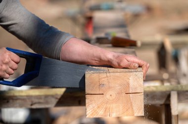 Bir insan, dışarıdaki tezgahta gün ışığında tahta bir bloğu kesmek için el testeresi kullanır..