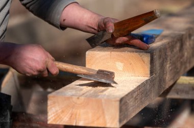Ahşap işçisi gün ışığında keski ve çekiç kullanarak tahta kirişi şekillendirir..