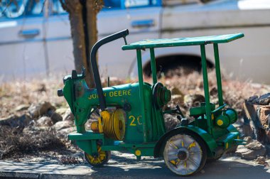 Skrunda, Letonya - 22 Mart 2025: Bir dekoratif yeşil traktör modeli kayalar ve güneş ışığıyla çevrili bir taş yolda duruyor.