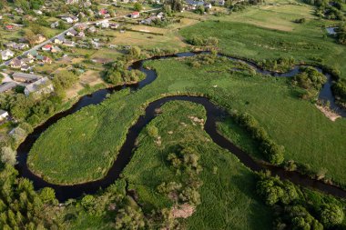 Resimli bir nehir, sakin bir kırsal alanda canlı yeşillikler arasında kıvrılır..