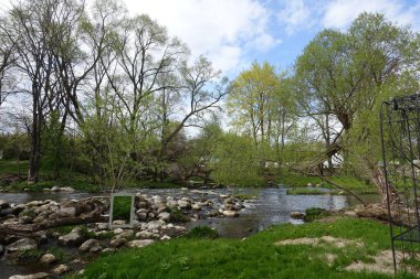 Sıcak bir günde, parçalı bulutlu bir gökyüzünün altında yeşil ve kayalıklarla çevrili akan nehir.
