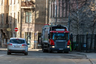 Riga, Letonya - 2 Mart 2021: Durağan bir aracın yakınındaki işlek bir caddede ağır yük kamyonu atık topluyor.