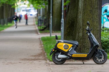 Riga, Letonya - 29 Mayıs 2021: İnsanlar geçerken ağaçlarla dolu bir patikada park edilmiş bir elektrikli scooter bulundu.