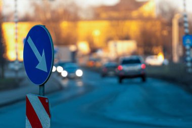 Ön planda belirgin bir trafik işareti dururken, arabalar yol boyunca sürüyorlar