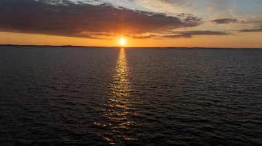 Canlı bir günbatımı, gün geceye geçerken, suyun üzerinde sıcak renkler bırakır..