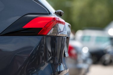 Güneşli bir günde kalabalık bir otoparkta park halindeki bir arabanın parlak kırmızı arka lambası belirir..