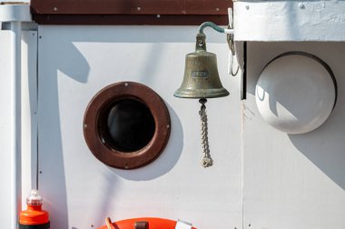 Pirinç çan yuvarlak bir pencere deliğinde asılı, deniz tasarımı ve dokuları vurgulanıyor.