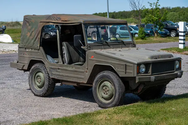 Engebeli bir askeri araç güneşli bir açık alanda park halinde. Etrafı yeşilliklerle çevrili..