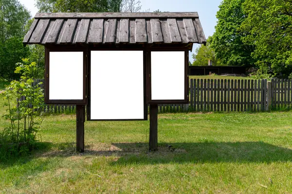 Boş bilgilendirme tahtası çimlerin üzerinde ağaçlarla ve arka planda ahşap bir çitle oturur..