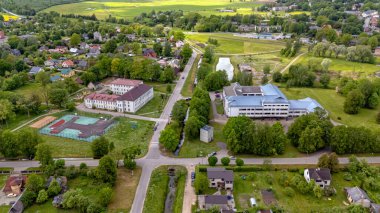 Auce, Letonya - 31 Mayıs 2025: Yeşillik çevresi binalar, yollar ve yakınlarındaki küçük bir gölet ile çevrili.