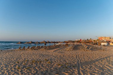 Yunanistan 'ın Girit kentindeki sakin kumlu sahil, deniz kenarında şezlonglar ve şemsiyelerle.