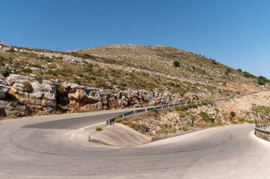 Yunanistan 'ın Girit kentinde açık mavi gökyüzünün altında kayalık tepelerle çevrili virajlı yol.