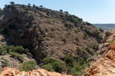 Ziyaretçiler açık mavi gökyüzünün altındaki Girit 'teki Milatos Mağarası' nı çevreleyen engebeli araziye hayran..