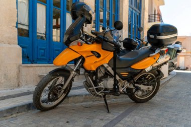 Girit 'te mavi bir kapının yanında park etmiş parlak turuncu bir motosiklet yerel cazibesini sergiliyor..
