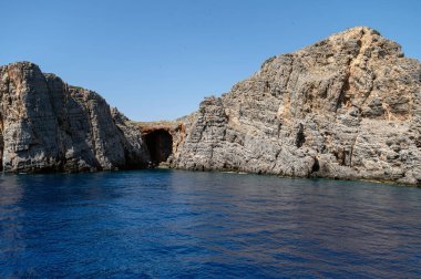 Ziyaretçiler güneşli bir günde ışıl ışıl denizin tadını çıkarırken Girit 'in engebeli uçurumlarına hayran kalırlar..