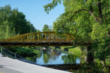 Güneşli bir günde yemyeşil sularla çevrili sakin bir nehri kaplayan renkli bir köprü.