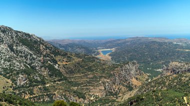 Bereketli yeşil dağlar dolambaçlı bir nehre ve berrak bir gökyüzünün altındaki sakin denize bakar..