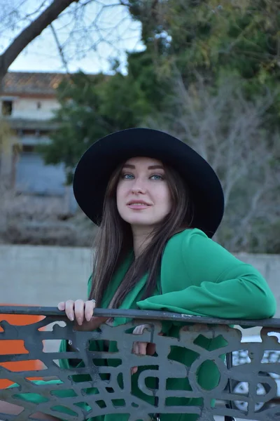 公園でポーズをとっている帽子と黒いドレスを着た美しい若い女性 — ストック写真