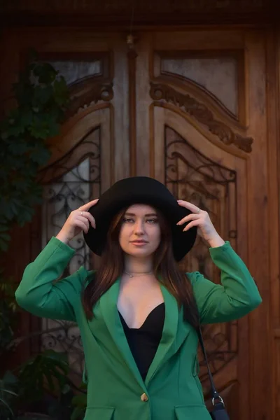 Красивая Молодая Женщина Шляпе Черном Пальто Позирует Фоне Деревянного Дома — стоковое фото