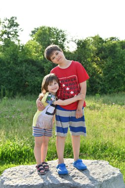 İki çocuk bir manzaranın arka planında oturuyor.,