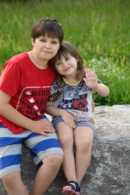 İki çocuk bir manzaranın arka planında oturuyor.,