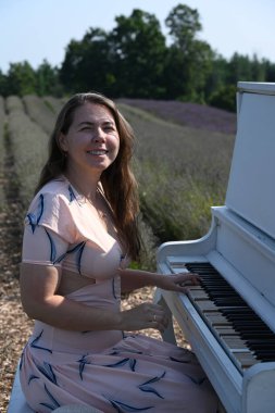 Lavanta tarlasında beyaz elbiseli bir kız piyanonun başında oturuyor.,