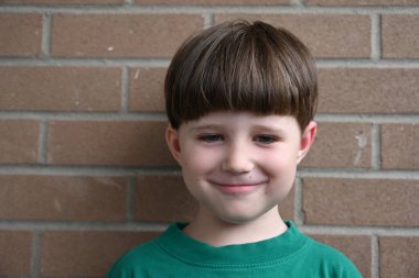 Tuğla duvarın yanında kısa saçlı şirin bir çocuğun portresi.