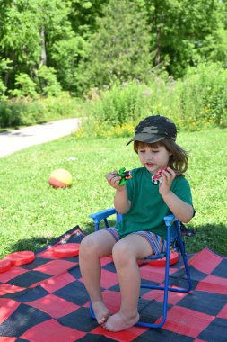 Parktaki sandalyede oturan ve küçük arabalarla oynayan uzun saçlı tatlı çocuk.