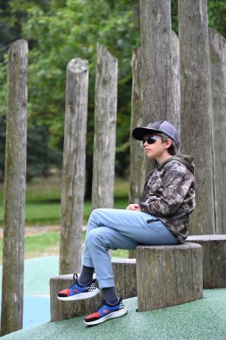 Parktaki bir çocuk parkta bankta oturuyor.,